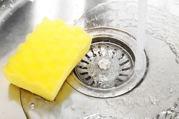 Yellow sponge in a sink with running water